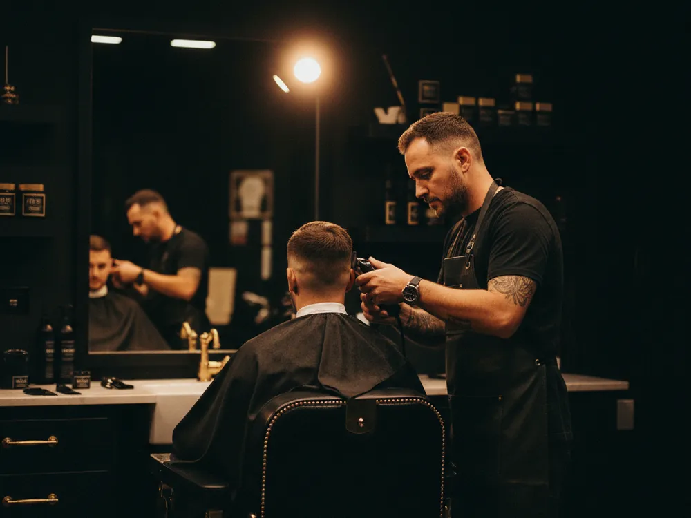 A barber mid-cut in a busy shop, a second chair working behind him