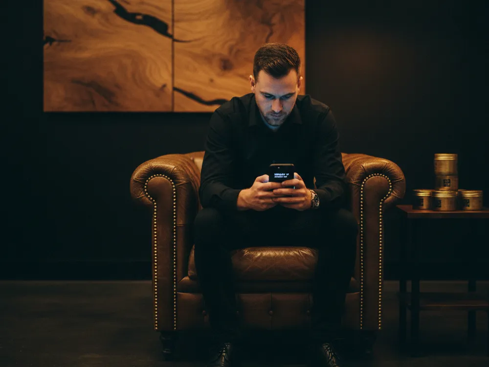 A customer waiting in an armchair, watching his place in the queue on his phone